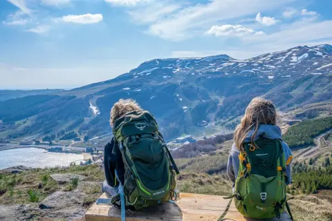 Deux randonneurs contemplent le paysage depuis le Puy de Chambourguet. Le lac scintille, les montagnes enneigées se dressent à l'horizon.