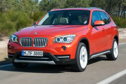 Pomarańczowy BMW X1 E84 jedzie po drodze, za kierownicą siedzi mężczyzna.