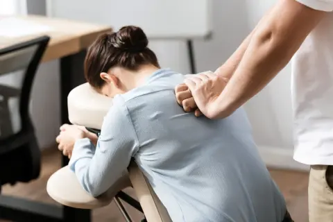 Un masseur offre des massages en entreprise à une femme assise sur une chaise ergonomique, soulageant les tensions du dos.