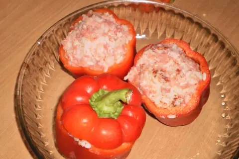 Trzy czerwone papryki faszerowane surowym mięsem mielonym i ryżem, gotowe do pieczenia.