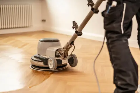 Ein Handwerker versiegelt einen Parkettboden mit einer Poliermaschine. Der frisch versiegelte Boden glänzt.