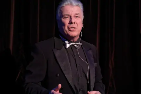 Emilian Kamiński w czarnym smokingu z muszką, jakby opowiadał o swoich filmach.