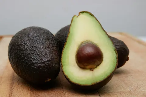 Dwa całe awokado i jedno przekrojone na pół, z widocznym pestką. Idealne do zdrowej diety, choć awokado kcal warto znać.