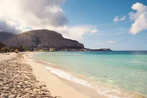 Piękna plaża Mondello z turkusową wodą, piaszczystym brzegiem i malowniczym miasteczkiem u podnóża góry.