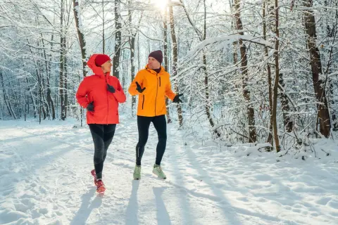 Un couple profite de l'air frais en courant sous la neige dans une forêt enneigée.