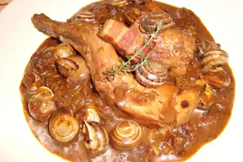 Guiso de conejo con caracoles, bañado en una rica salsa oscura, con trozos de tocino y una ramita de romero.