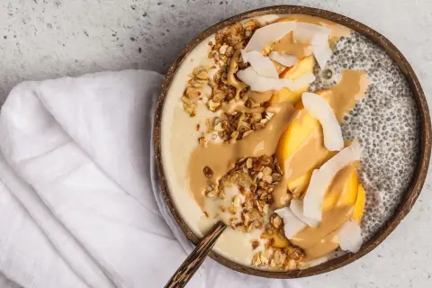 Cremige Chia Overnight Oats im Kokosnussschalen-Bowl mit Pfirsich, Granola und Erdnussbutter. Ein gesunder Start in den Tag!