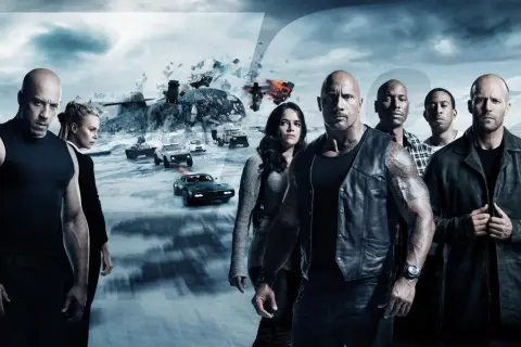 Die Hauptdarsteller der besetzung von Fast & Furious 8 stehen vor einer eisigen Landschaft mit explodierenden Fahrzeugen und einem Helikopter.