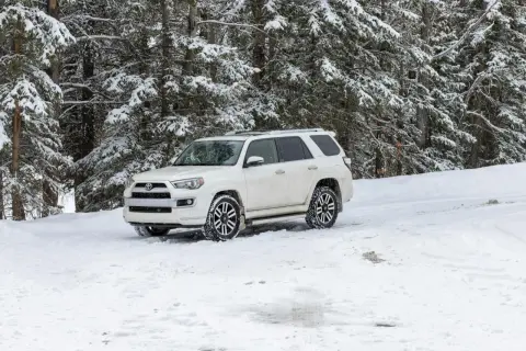 Biały SUV z napędem **awd** stoi na zaśnieżonej drodze w lesie.