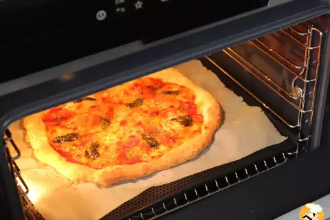Une pizza maison dorée et appétissante est en pleine cuisson dans un four moderne. Le fromage fond et les herbes parfument l'air.