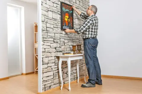 Mann hängt Bild an Trockenbauwand. Ein Mann baut eine Trockenbauwand und dekoriert sie mit einem Bild.