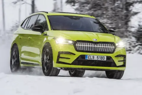 En ljusgrön Skoda Enyaq testas i snö. Bilen kör genom ett vinterlandskap med träd i bakgrunden.