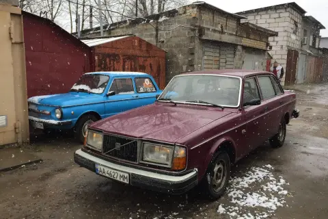 En vinröd Volvo 244 DLS står parkerad bredvid en blå bil i snöfall.