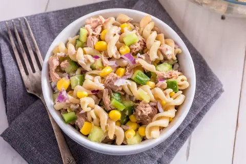 Ein köstlicher nudelsalat mit thunfisch, garniert mit Mais, Gurken und roten Zwiebeln, bereit zum Genießen.