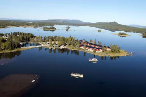 Vacker vy över en sjö med röda byggnader och båtar vid **kraja Arjeplog**.