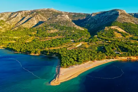 Idealne miejsce, gdzie na wakacje w lipcu: piaszczysta plaża otoczona zielenią, góry w tle i turkusowe morze.