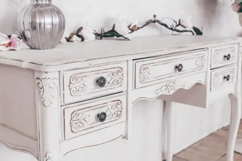 Un mobile da marrone a bianco, con dettagli intagliati e pomelli antichi. Un vaso d'argento e fiori decorano il piano.