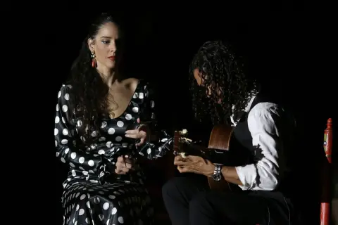 Unos buenos días flamencos con una bailaora y un guitarrista en un escenario oscuro.