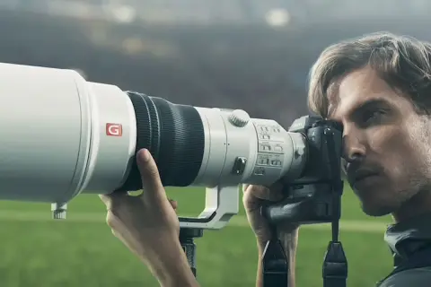 Photographe sportif utilisant un appareil photo Sony a9 II avec un téléobjectif blanc, prêt à capturer l'action sur le terrain.