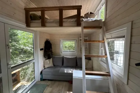 Clevere tiny house bett ideen: ein gemütliches Hochbett über einer Couch, mit Leiter und Fensterblick ins Grüne.