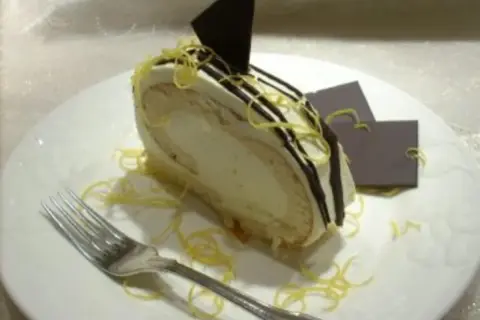 Ein Stück Zitronenrolle mit cremiger Füllung, dekoriert mit Schokoladenglasur und Zitronenzesten. Ein perfektes Zitronenrolle Rezept zum Nachbacken.