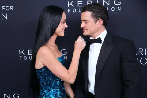 Katy Perry i Orlando Bloom patrzą na siebie z czułością. Ona w błyszczącej sukni, on w eleganckim smokingu.
