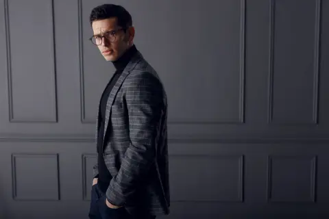Elegancki mężczyzna w okularach, w kratowaną marynarkę i czarny golf, który stanowi idealny sweter pod marynarkę.