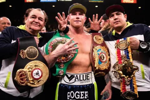 Canelo Alvarez, surrounded by his team, proudly displays multiple championship belts, a testament to his impressive boxing record.