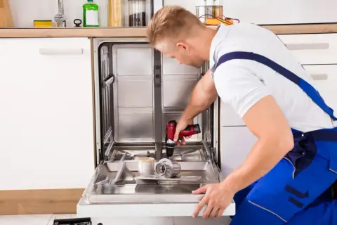 Fachowiec przykręca front do zmywarki, używając wiertarko-wkrętarki.