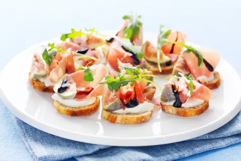 En tallrik med läckra crostini med lufttorkad skinka, färska fikon, krämig ost och ruccola, ringlad med balsamvinäger.