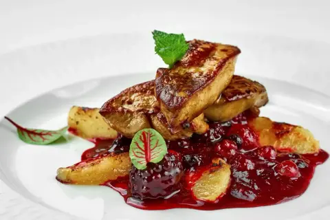 Tranches de foie gras poêlé, nappées d'une sauce aux fruits rouges, garnies d'une feuille de menthe et d'une petite feuille rouge. L'épice foie gras est sublimée par cette présentation.