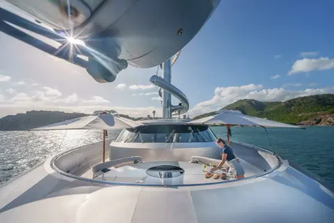 Un membro dell'equipaggio prepara un rinfresco sul ponte del Maltese Falcon yacht, con il sole che splende sull'acqua cristallina.