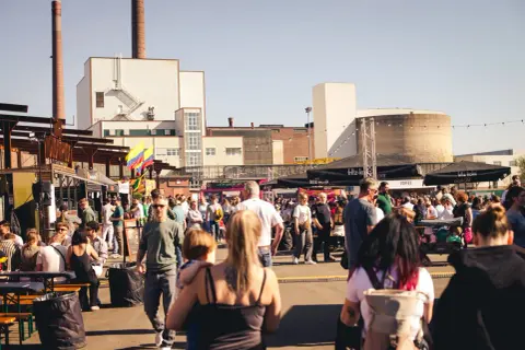 Menschen genießen das Street Food Festival Bergisch Gladbach mit vielen Essensständen und bunter Atmosphäre vor Industriebauten.