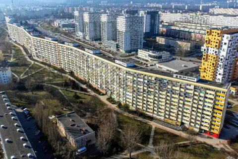 Długi, falisty budynek mieszkalny, znany jako falowiec gdańsk, otoczony zielenią i innymi blokami.