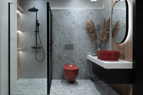 Mała łazienka w stylu loftowym z czerwoną misą WC i umywalką, szarymi płytkami i czarną armaturą.