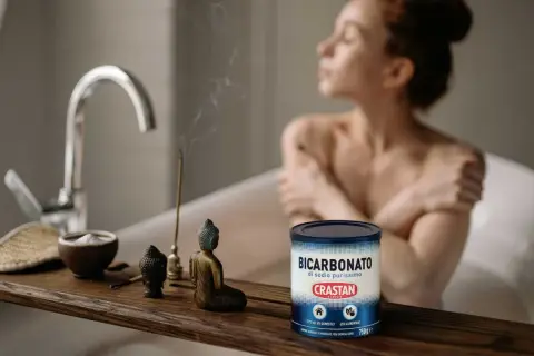 Una donna rilassata in vasca da bagno, con incenso e una ciotola di bicarbonato di sodio purissimo, un prodotto versatile per la casa e l'alimentazione.
