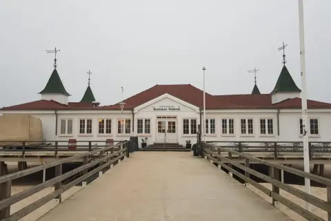 Historyczna budowla na molo w Ahlbecku, z charakterystycznymi zielonymi dachami i białymi ścianami, zaprasza do spaceru.