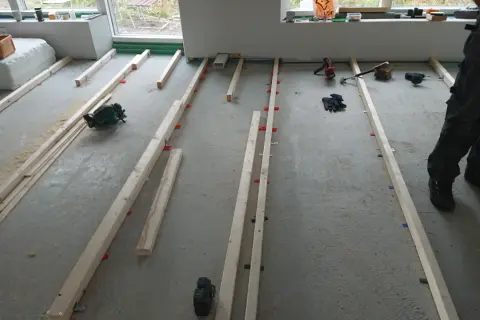 Arbetare förbereder för att regla upp golv med träreglar och verktyg som cirkelsåg och skruvdragare.
