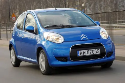 Niebieski Citroen C1 pędzi po drodze, odbijając światła miasta w swoich błyszczących reflektorach.