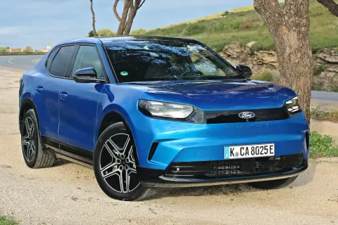 Niebieski Ford Capri 2025, nowoczesny elektryczny SUV, zaparkowany na żwirowej drodze obok drzewa.