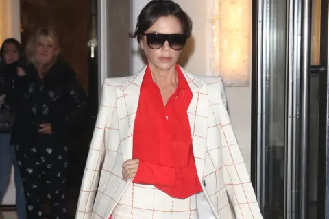Victoria Beckham, con un traje de cuadros blanco y naranja y camisa roja, sale de un edificio.