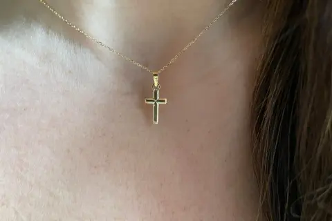 Una delicada cadena de oro sostiene una cruz de oro pequeña, un símbolo de fe y elegancia.