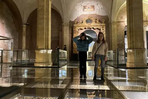 Due ragazze esplorano il Palazzo Madama, con un pavimento in vetro che rivela antiche rovine sottostanti.