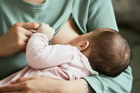 Mama karmi dziecko. Piersi są pełne mleka, co może powodować uczucie twardości przy karmieniu.