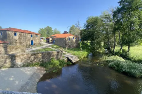 Casas de piedra con tejados rojos y ventanas azules junto a un río. Un lugar idílico que ver en Vila de Cruces.