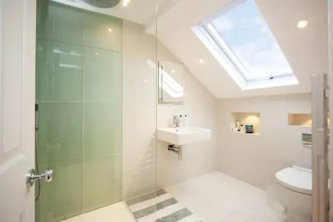 Moderno baño con ducha de cristal verde, lavabo flotante y tragaluz. Ideas para como decorar un baño con estilo y luz natural.