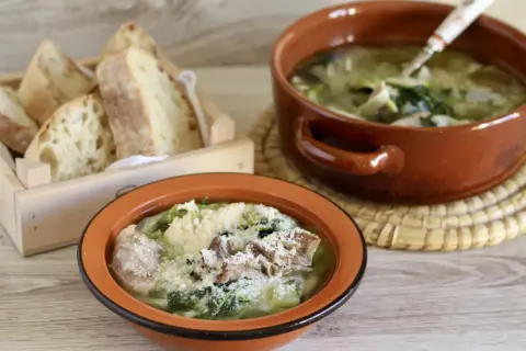 Two bowls of hearty Italian soup with greens and meat, served with crusty bread in a wooden crate.