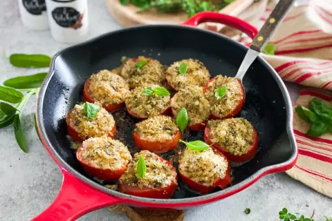 Pomodori gratinati in padella, ripieni di pangrattato e erbe aromatiche, guarniti con basilico fresco.