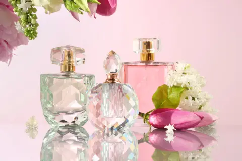 Trzy flakoniki perfum i kwiaty na różowym tle.