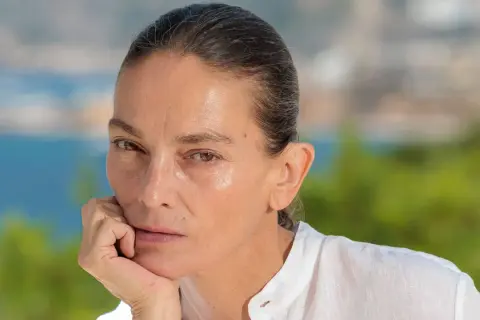 Retrato de **Laura Ponte joven**, con la mano apoyada en la barbilla, mirando pensativa. Fondo desenfocado de mar y vegetación.